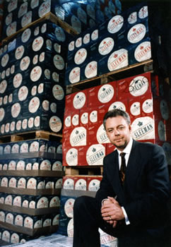 John W. Sleeman seated in front of a wall of Sleeman beer cases 2010-99 (Box 20)
