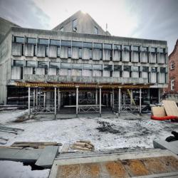 Large concrete slab at new library front entrance held up by support beams.