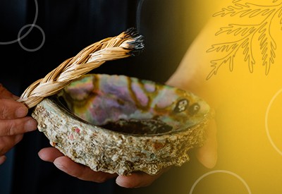 Hands hold an abalone shell and braided sweetgrass.