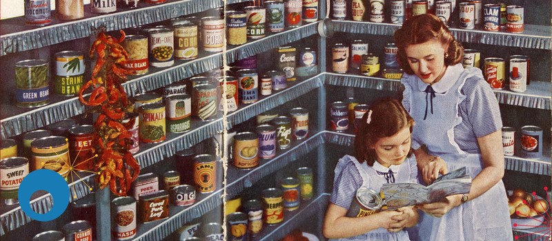 This image features a woman and a young girl looking at a recipe together, standing in front of metal shelving stocked with cans of food.